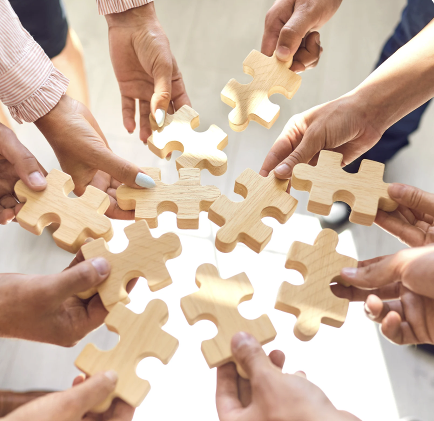 Viele Hände setzen gemeinsam Puzzleteile zusammen als Sinnbild für Teamwork